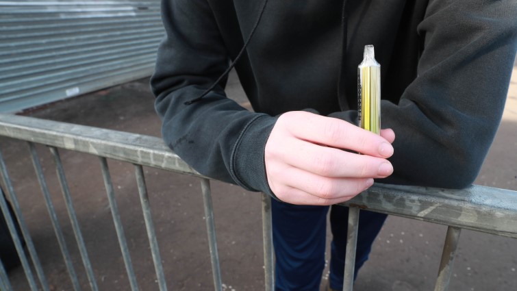 This is a photo of a young person holding a single use vape. Their face is not in shot.