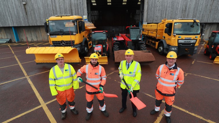 Councillor Robert Brown stands with three of the team from Canderside depot with the salt barn and two winter vehicles behind them.